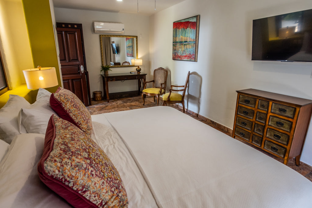 Neatly made bed in a room with a dresser, chair, and television.