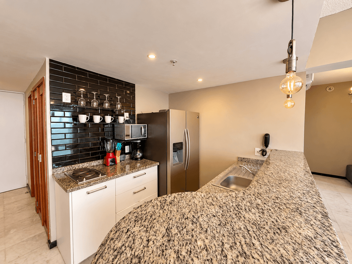Cocina amueblada con azulejo negro, refrigerador y barra de granito en departamento en venta en Park Royal Mazatlán