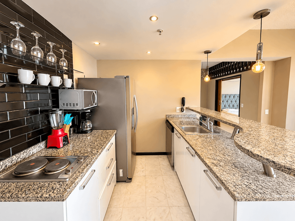 Cocina amueblada con azulejo negro, copas colgantes y barra de granito en departamento en Park Royal Mazatlán