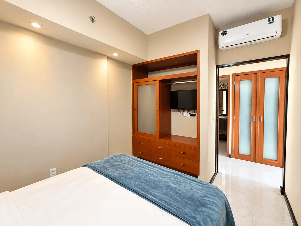 Recámara con mueble de madera con TV y aire acondicionado en departamento amueblado en Park Royal Mazatlán