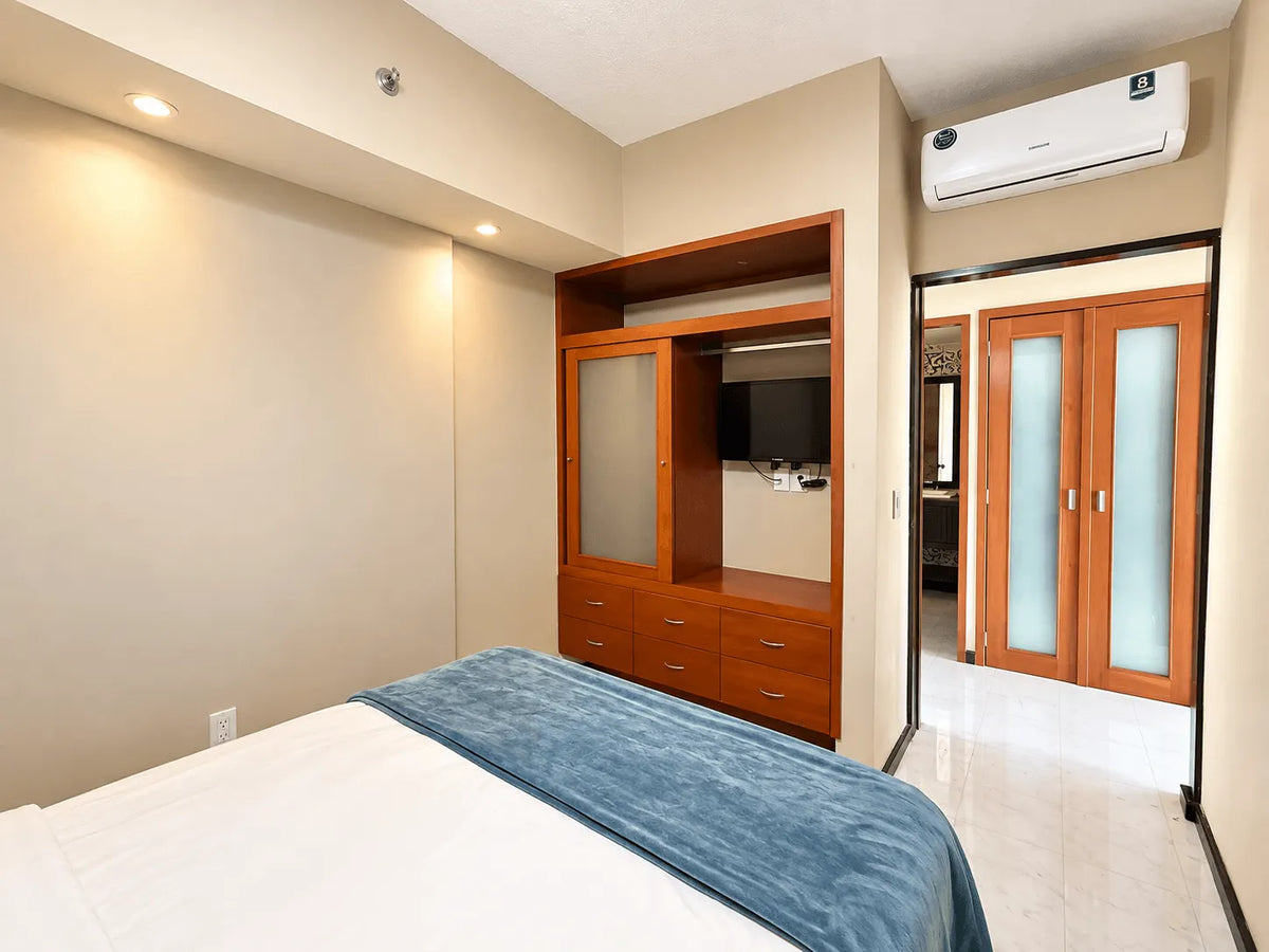 Recámara con mueble de madera con TV y aire acondicionado en departamento amueblado en Park Royal Mazatlán