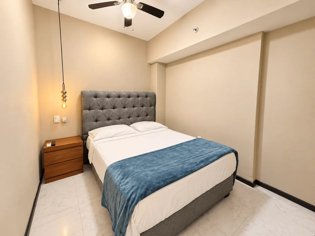 Recámara con cabecera capitoné, cobertor azul y buró de madera en departamento en venta en Park Royal Mazatlán