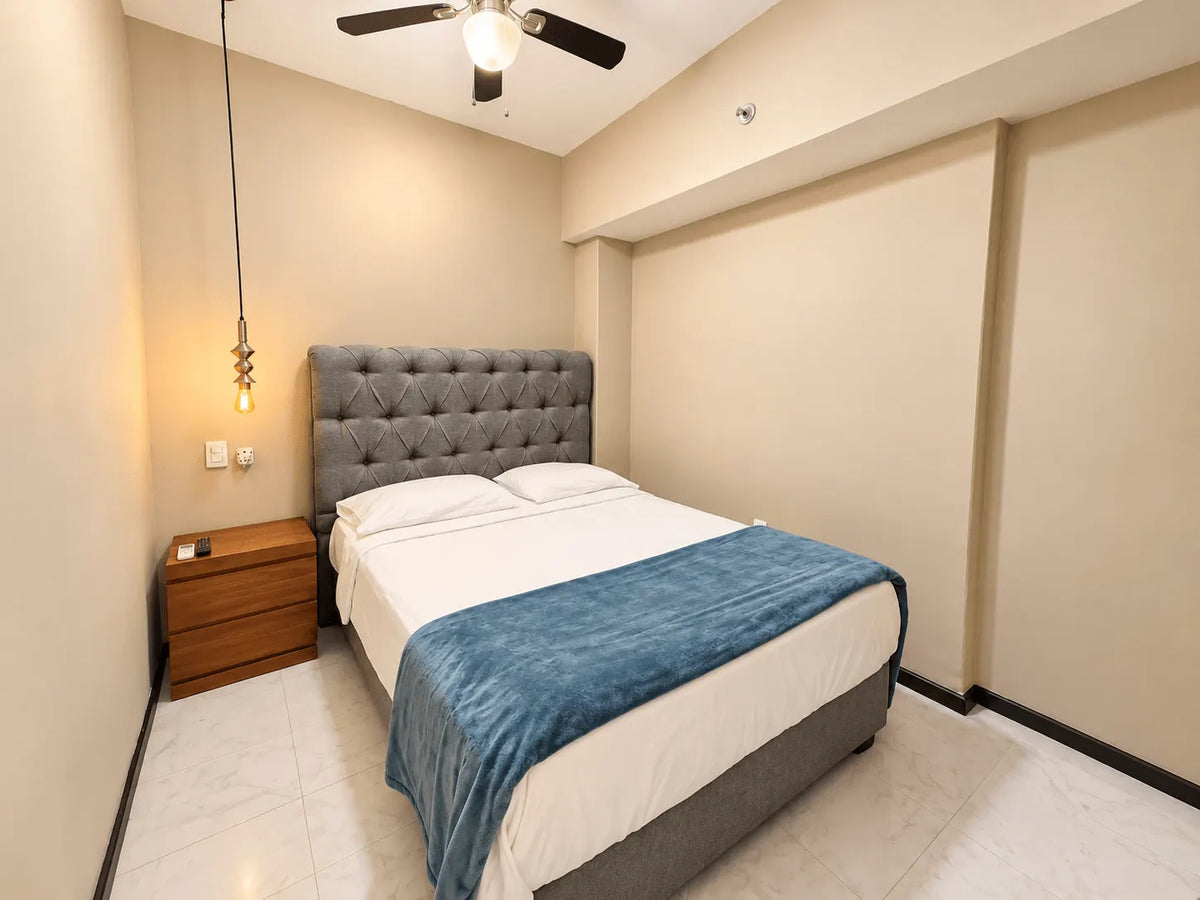 Recámara con cabecera capitoné, cobertor azul y buró de madera en departamento en venta en Park Royal Mazatlán