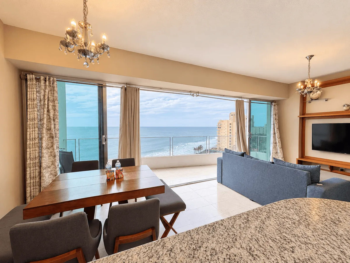 Comedor de madera y sala con candil y puertas corredizas hacia la terraza con vista al mar en Park Royal Mazatlán