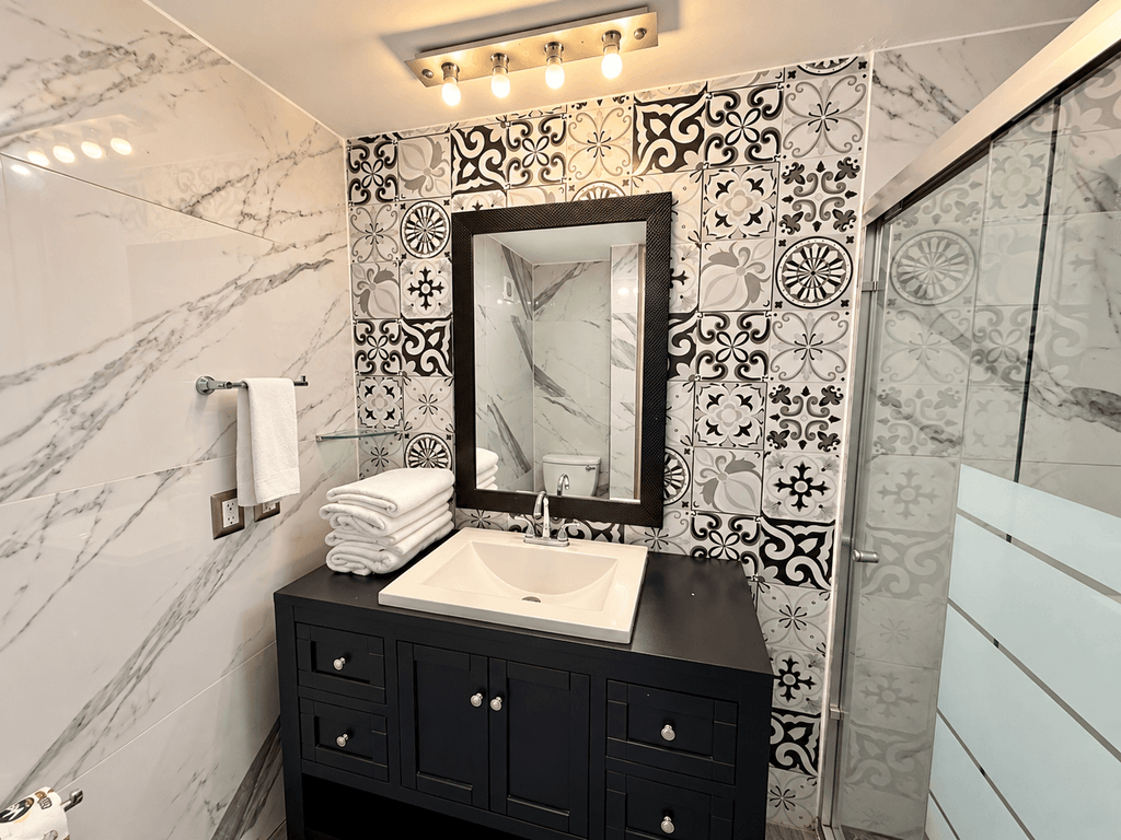 Baño con muros de mármol, mosaico decorativo y regadera de cristal en departamento en Park Royal Mazatlán