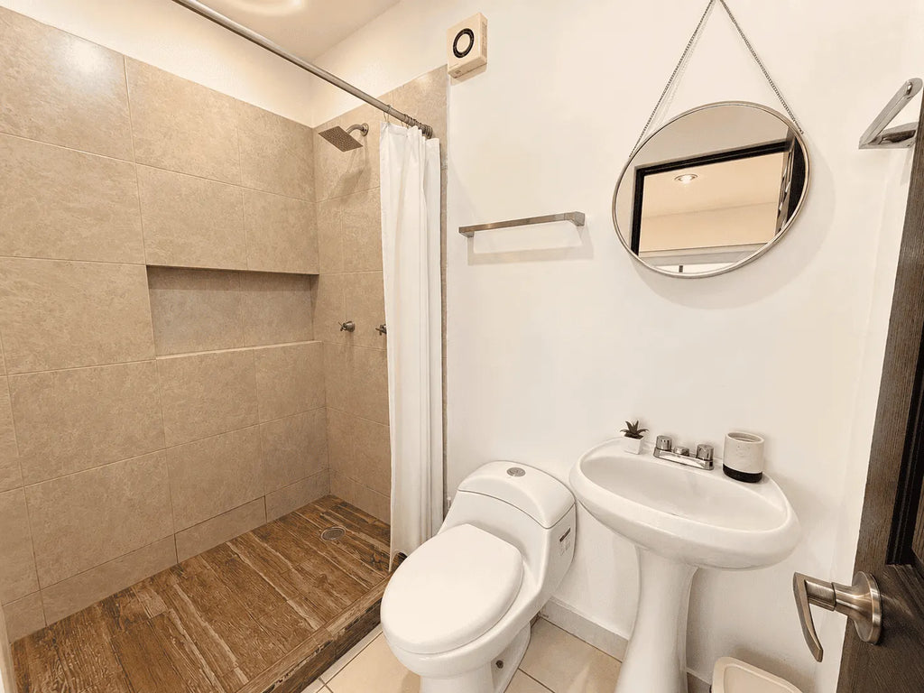 Baño completo con regadera, lavabo de pedestal y espejo redondo en departamento en venta en Cerritos, Mazatlán