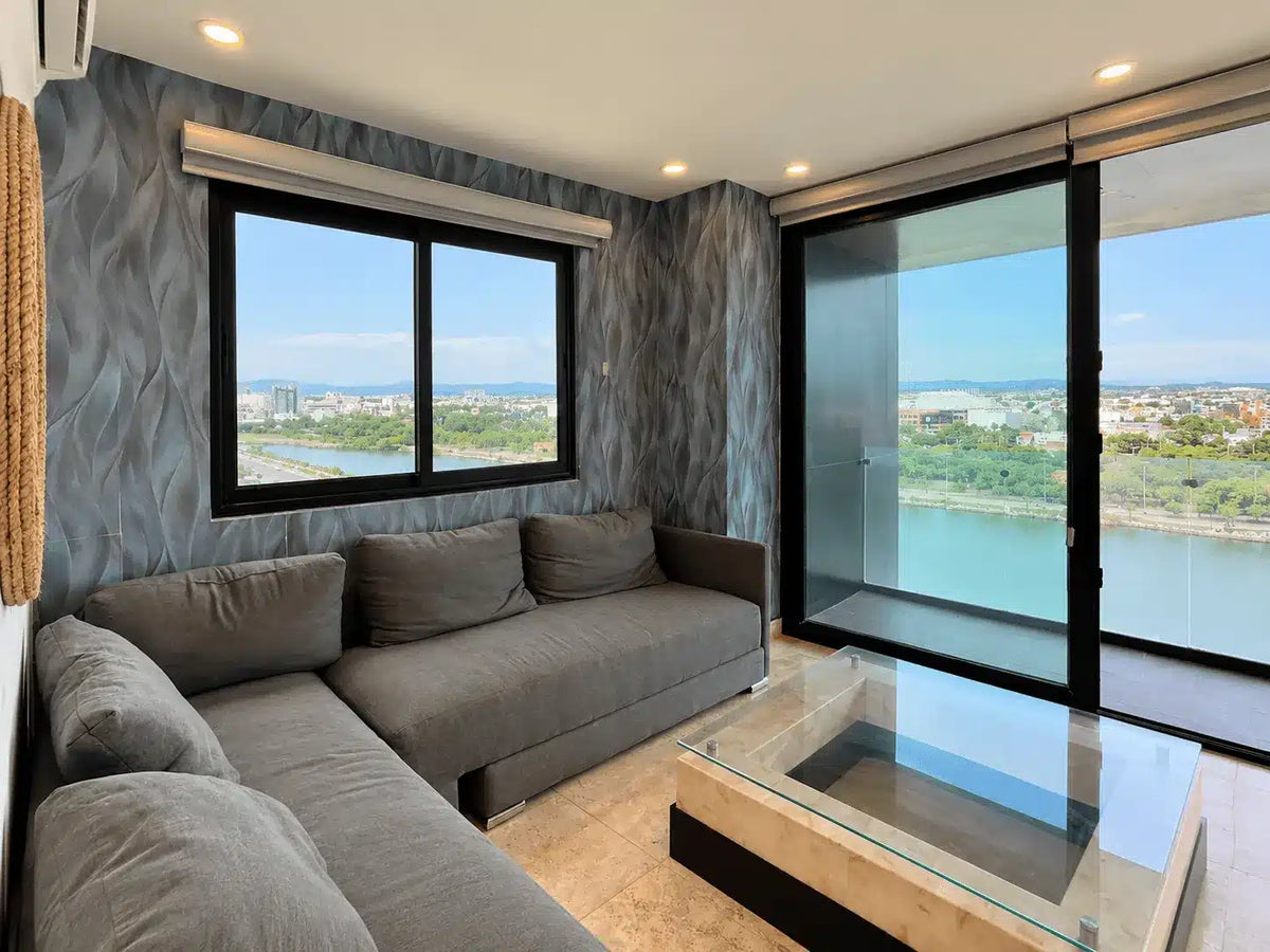 Sala con sofá gris y vista panorámica a la laguna, departamento en venta Malecón Mazatlán