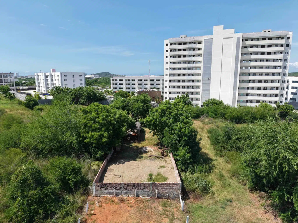 Vista aérea del terreno en esquina en Marina Universidad, Mazatlán, con edificio residencial al fondo